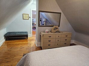 A bedroom with a bed, a dresser, a bench, and a mirror.
