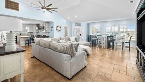 Ein geräumiger Wohnbereich mit grauem Sofa, Deckenventilator und einer Küche im Hintergrund.