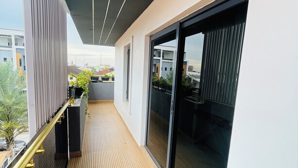 A modern balcony with a wooden floor, metal railing, and large sliding glass doors. - The GlobalNomad Enterprise (Lekki)
