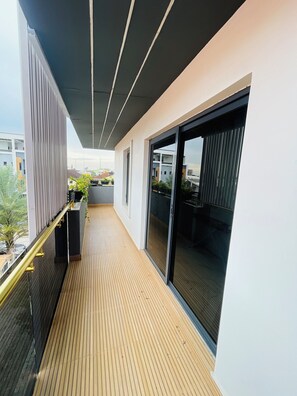Un balcón moderno con piso de madera, baranda metálica y grandes puertas corredizas de vidrio.