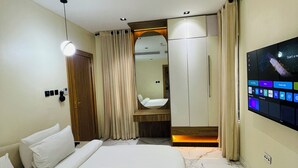 A hotel room with a large bed, a TV mounted on the wall, a vanity with a mirror, and a ceiling light. - The GlobalNomad Enterprise (Lekki)