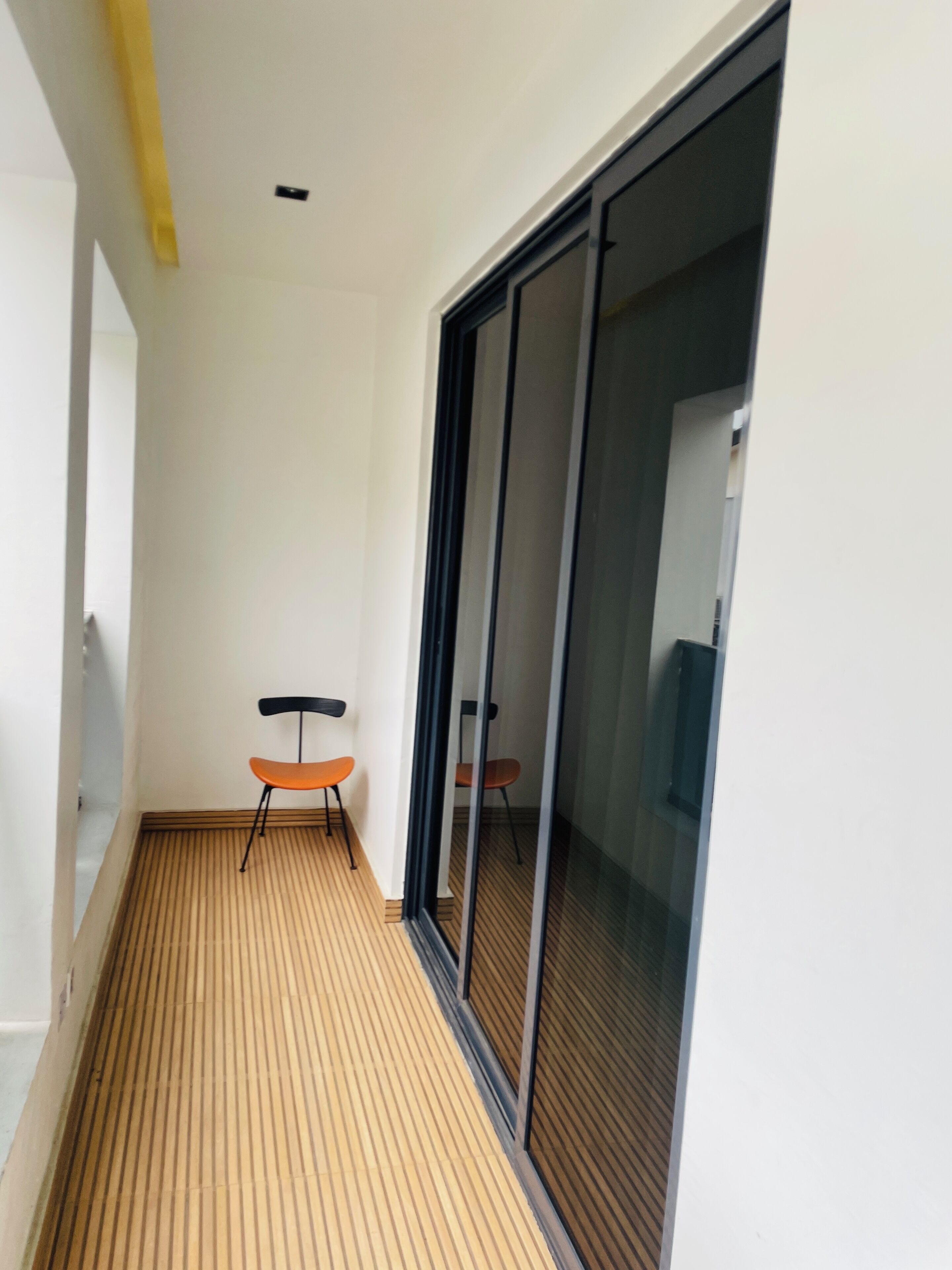 A narrow corridor with a wooden floor, a sliding glass door, and two chairs.