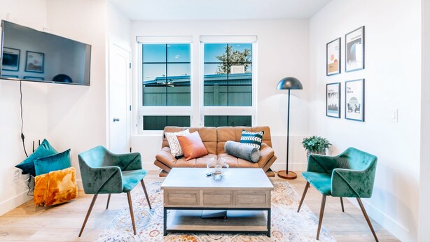 Ein modernes Wohnzimmer mit einem braunen Sofa, zwei grünen Sesseln, einem Holztisch und einem großen Fenster mit Blick auf ein Gebäude.