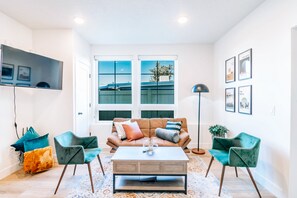 Ein modernes Wohnzimmer mit einem braunen Sofa, zwei grünen Sesseln, einem Holztisch und einem großen Fenster mit Blick auf ein Gebäude.