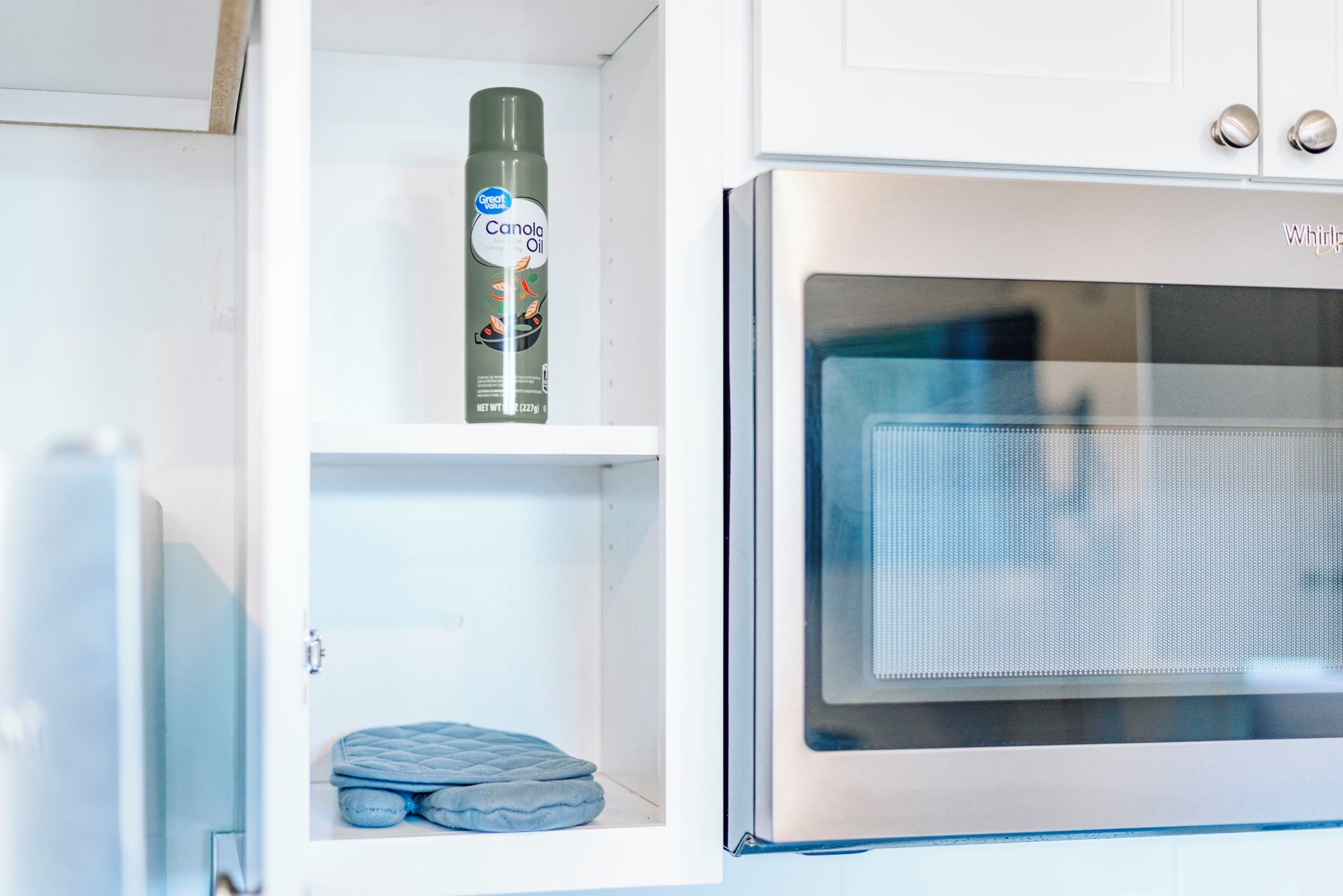 Uma cozinha com micro-ondas, uma prateleira com um óleo e um objeto acolchoado azul.