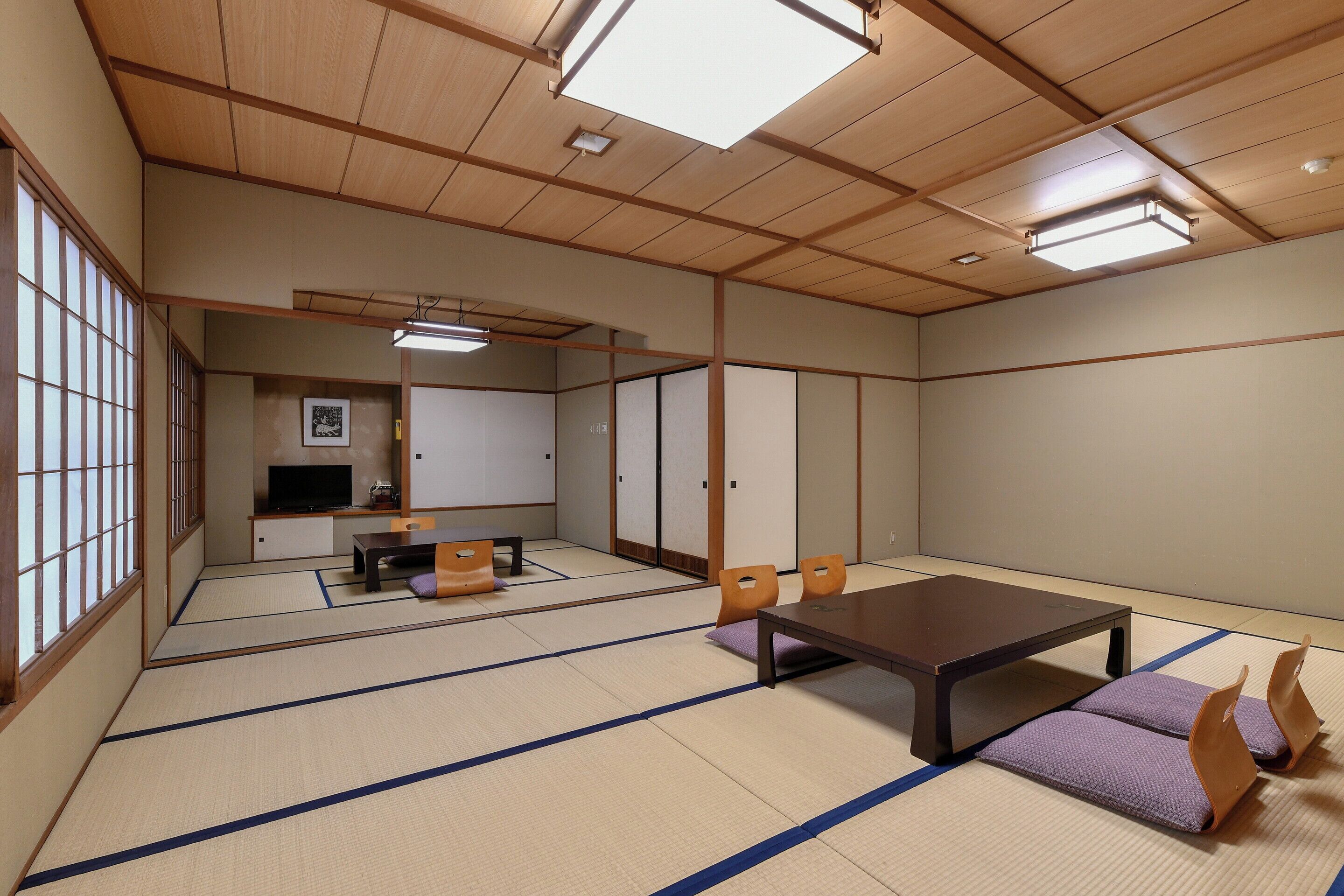 A tatami mat room with a low table, chairs, a television, and sliding doors.