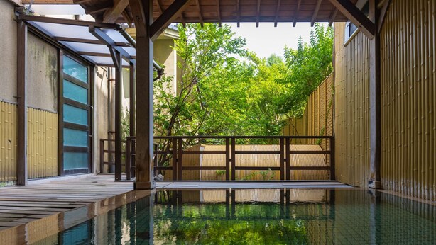 Ein traditionelles japanisches Onsen mit einer Holzterrasse, einem Steinbad und einem Bambuszaun.