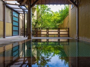Un onsen japonés tradicional con una terraza de madera, una tina de piedra y una valla de bambú.