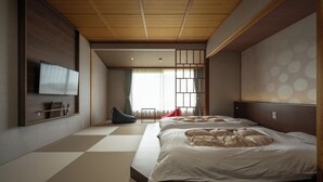 A room with tatami flooring, a bed with white bedding, a television mounted on the wall, and a sliding door with a view of the outside. - Awara Onsen Minoya Taiheikaku (Awara)