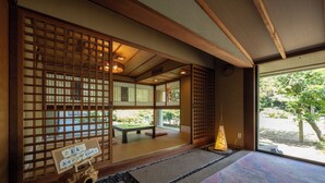 Ein traditioneller japanischer Raum mit Tatami-Bodenbelag, Schiebetüren und Blick auf Grünfläche.