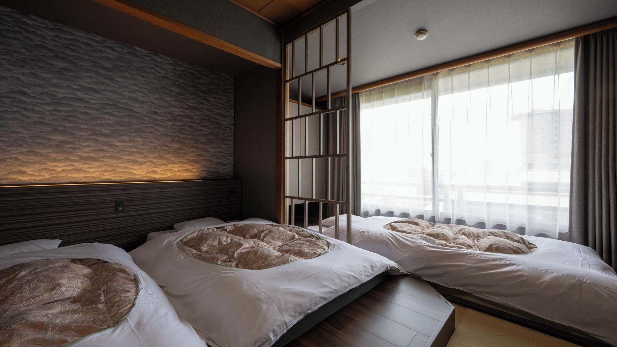 Habitación de hotel con un ventanal grande, una pared con textura y una cama con un cojín estampado.