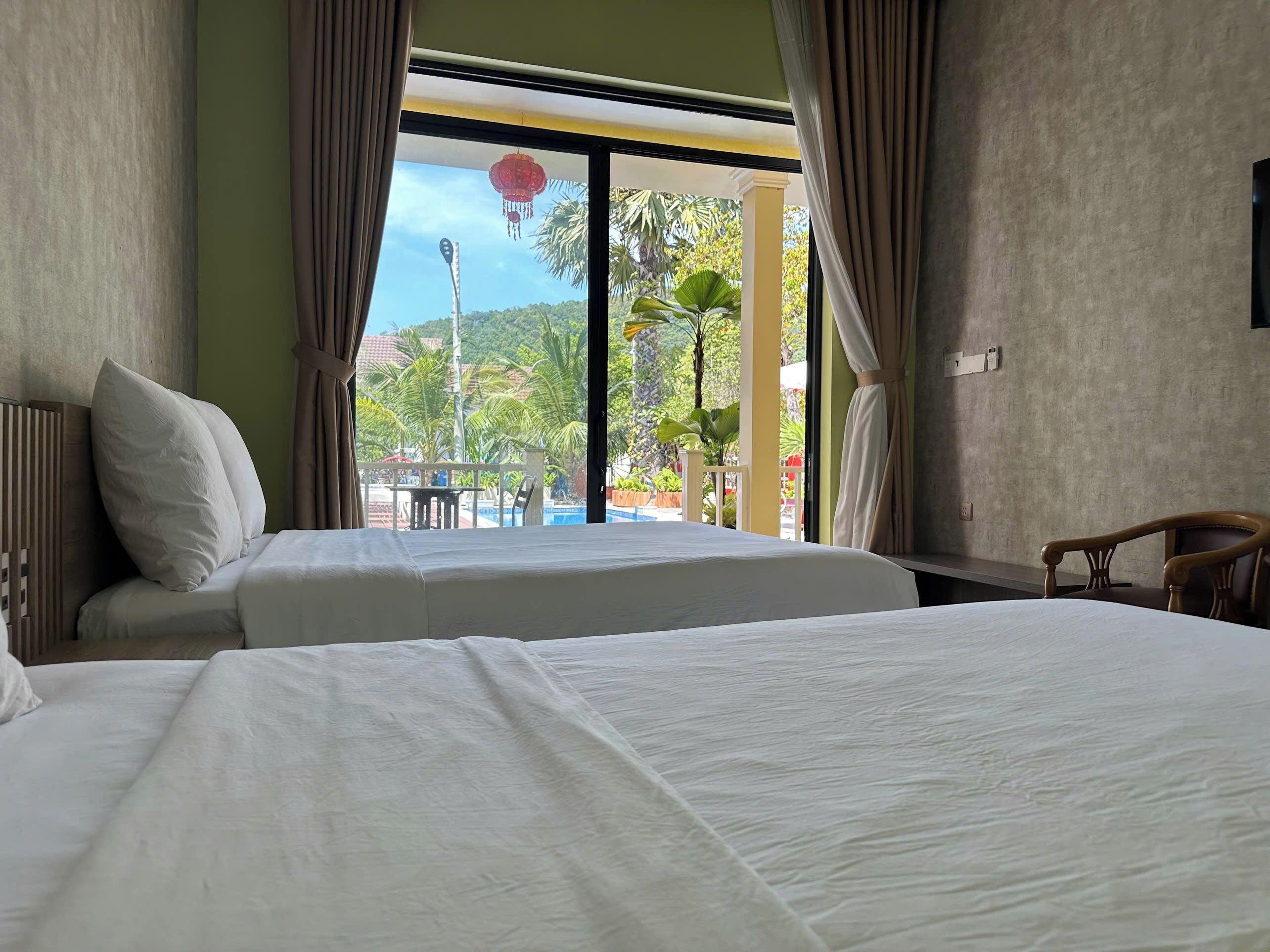 Une chambre d’hôtel avec deux lits, une vue sur une piscine et des palmiers, et un fauteuil.