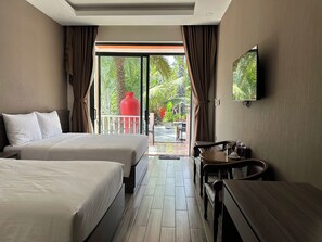 Hotelkamer met twee bedden, een eettafel, een televisie en een balkon met een rode pot en beplanting.