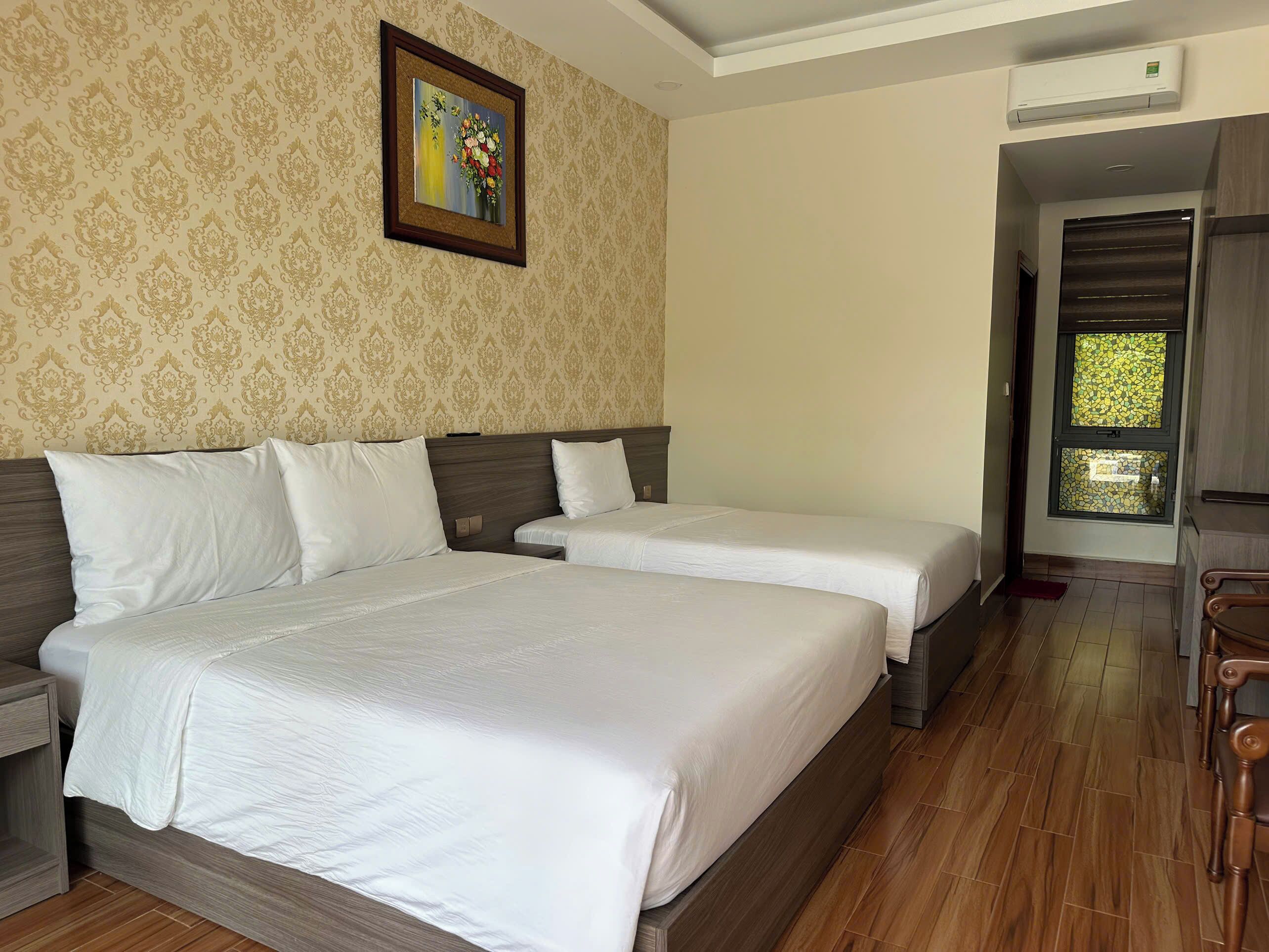 A hotel room with two beds, a wooden floor, a patterned wallpaper, and a framed artwork on the wall.