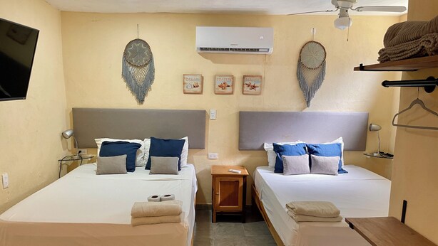 A room with two beds, a ceiling fan, an air conditioner, and wall decorations. - Downtown private Apartment w Kitchen (Isla Mujeres)