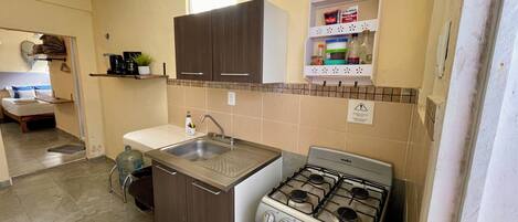 A compact kitchen with a gas stove, a sink, and a small countertop. There is a water dispenser and a cabinet above the sink.