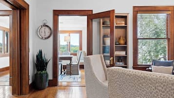 A living room with a sofa, a wooden floor, a bookshelf, and a view through an open door.