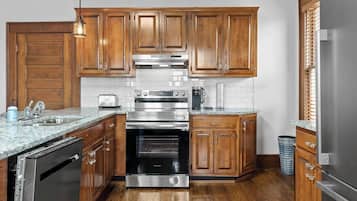 A kitchen with wooden cabinets, stainless steel appliances, a granite countertop, and a trash can.