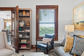 A living room with a bookshelf, a window with blinds, a sofa with patterned cushions, and a chair.
