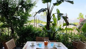 Un área de comedor al aire libre con una mesa lista para dos personas, rodeada de sillas y una planta grande en el centro.