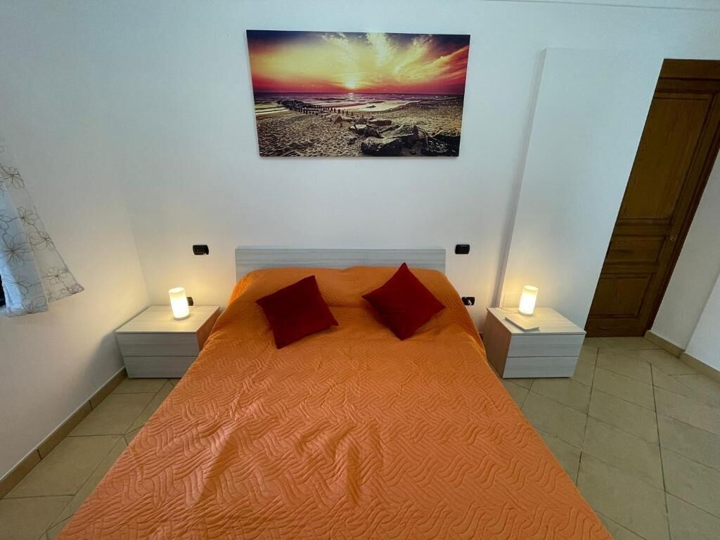 A bedroom with a large bed, two bedside tables with lamps, and a wall-mounted picture of a beach scene.