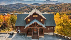 A log cabin with a porch, surrounded by autumn foliage and mountains in the background.