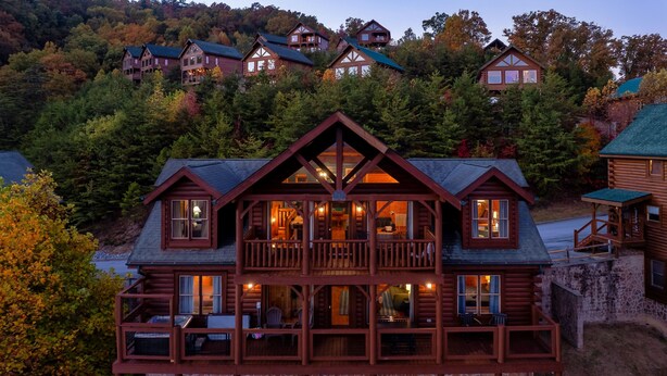 A multi-story log cabin with a balcony and a stone foundation.