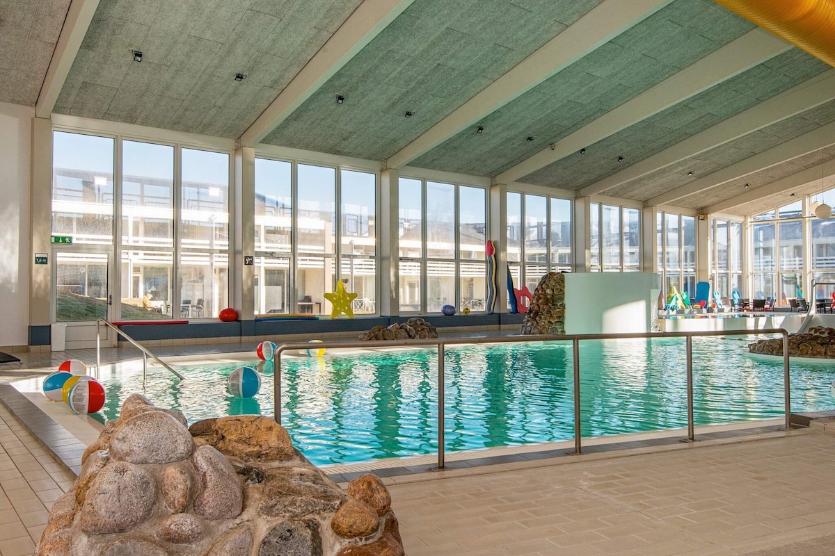 Ein Innenpool mit großen Glaswänden, einer Steinwand im Vordergrund und verschiedenen bunten Spielzeugen.