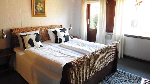 A bedroom with a large bed, a wooden headboard, a chandelier, a painting on the wall, and a window with curtains. - 2-person Room in a Hotel in Tranekaer (Tranekaer)