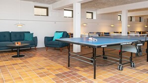 A ping pong table in a communal area with a tiled floor, sofas, and tables. - Apartment in Holiday Park- Shared Kitchen (Ulfborg)