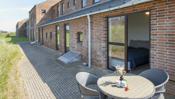 A modern brick building with a patio area featuring wicker chairs and a table. - Apartment in Holiday Park- Shared Kitchen (Ulfborg)