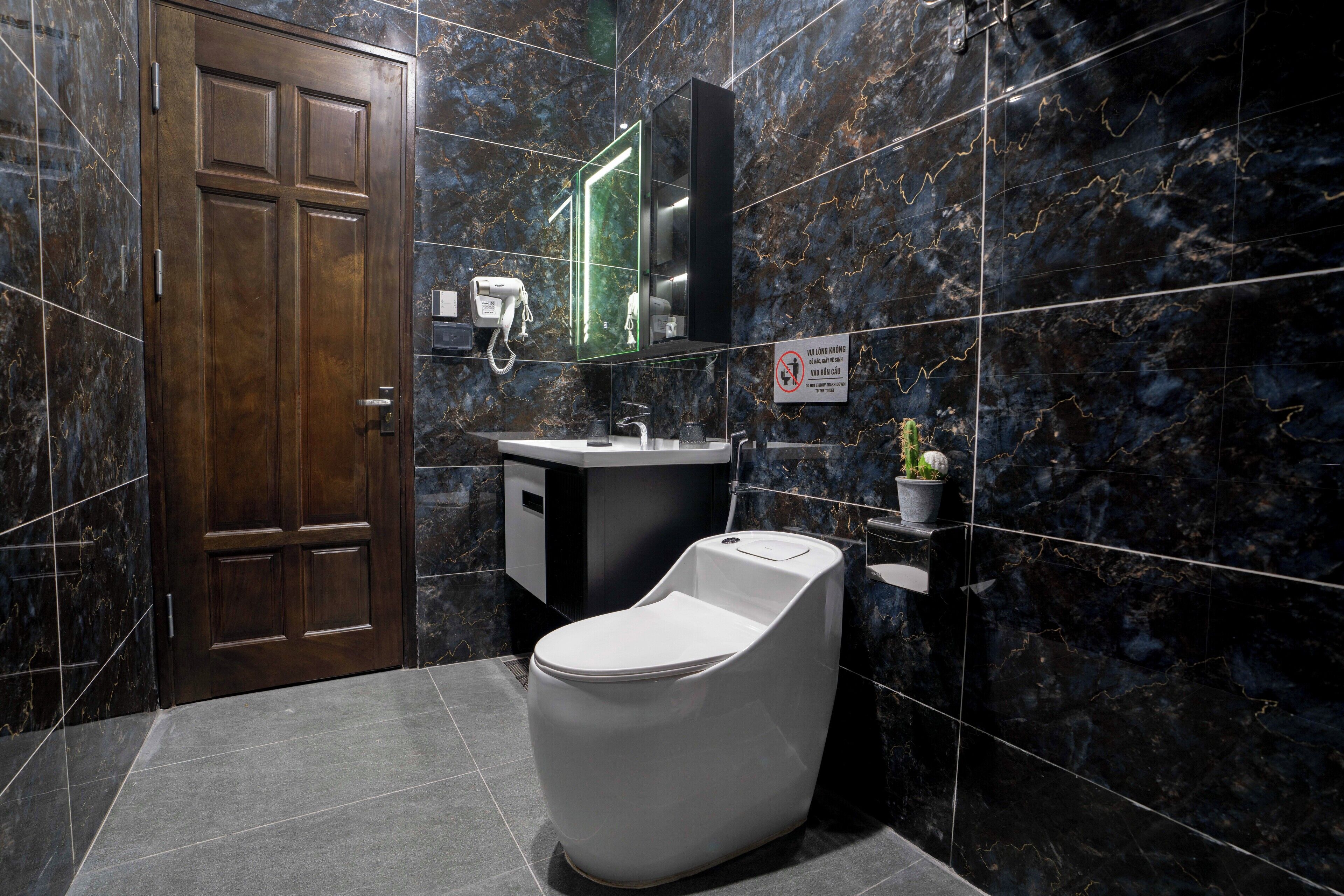 A modern bathroom with a marble wall, a wooden door, a white toilet, a sink, and a mirror.
