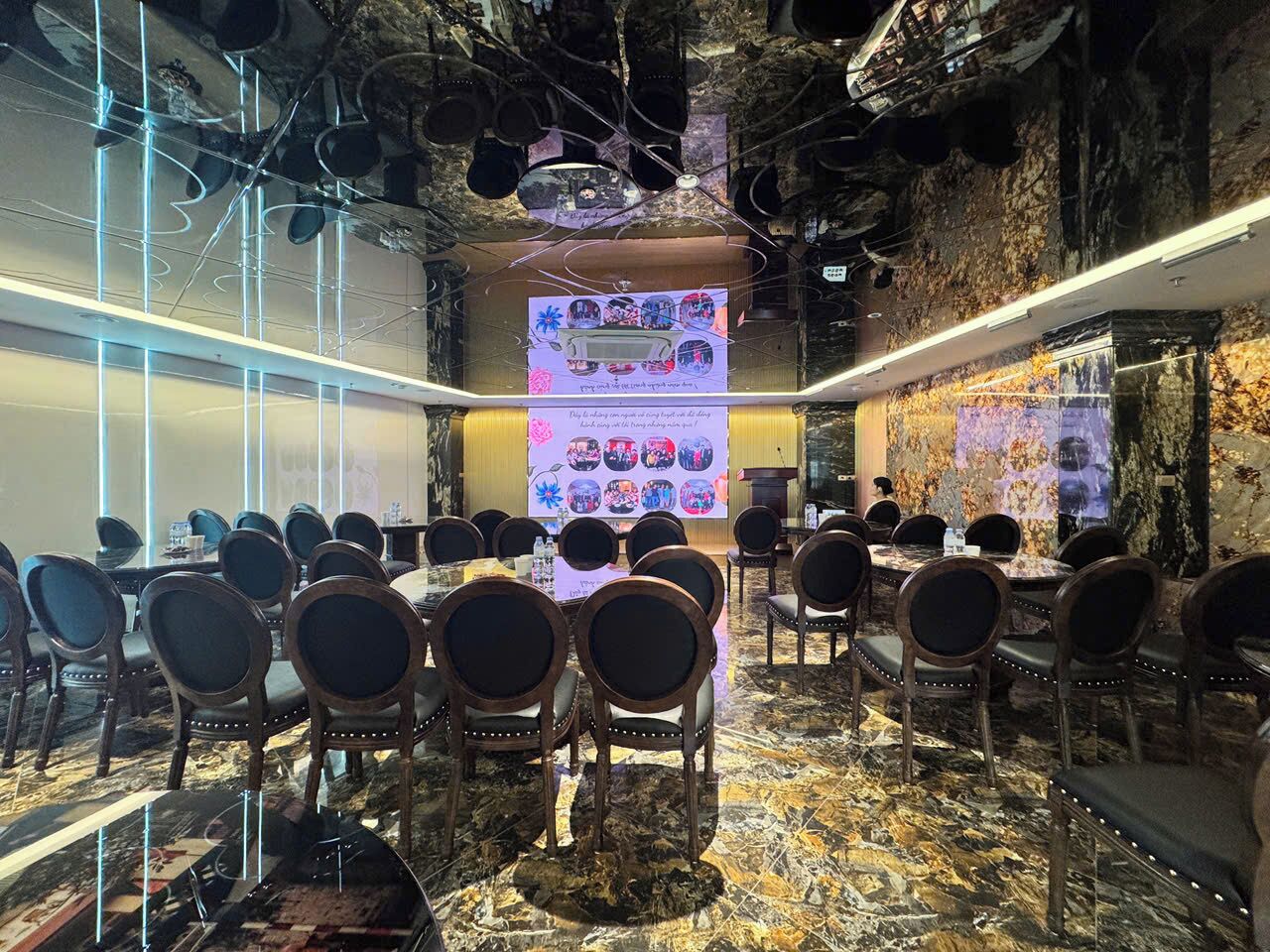 A conference room with tables and chairs, a presentation screen, and a decorative wall.