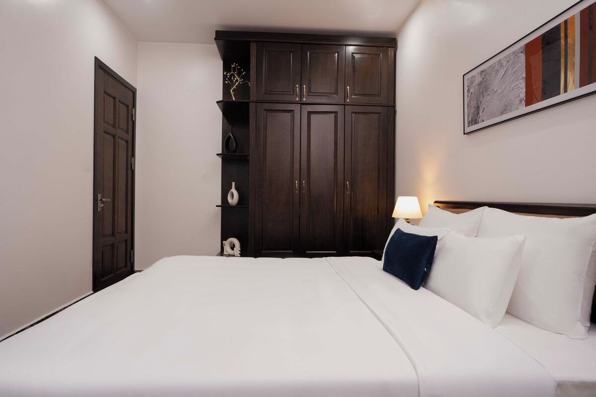 A hotel room with a large bed, dark wooden wardrobe, and a wall-mounted artwork.
