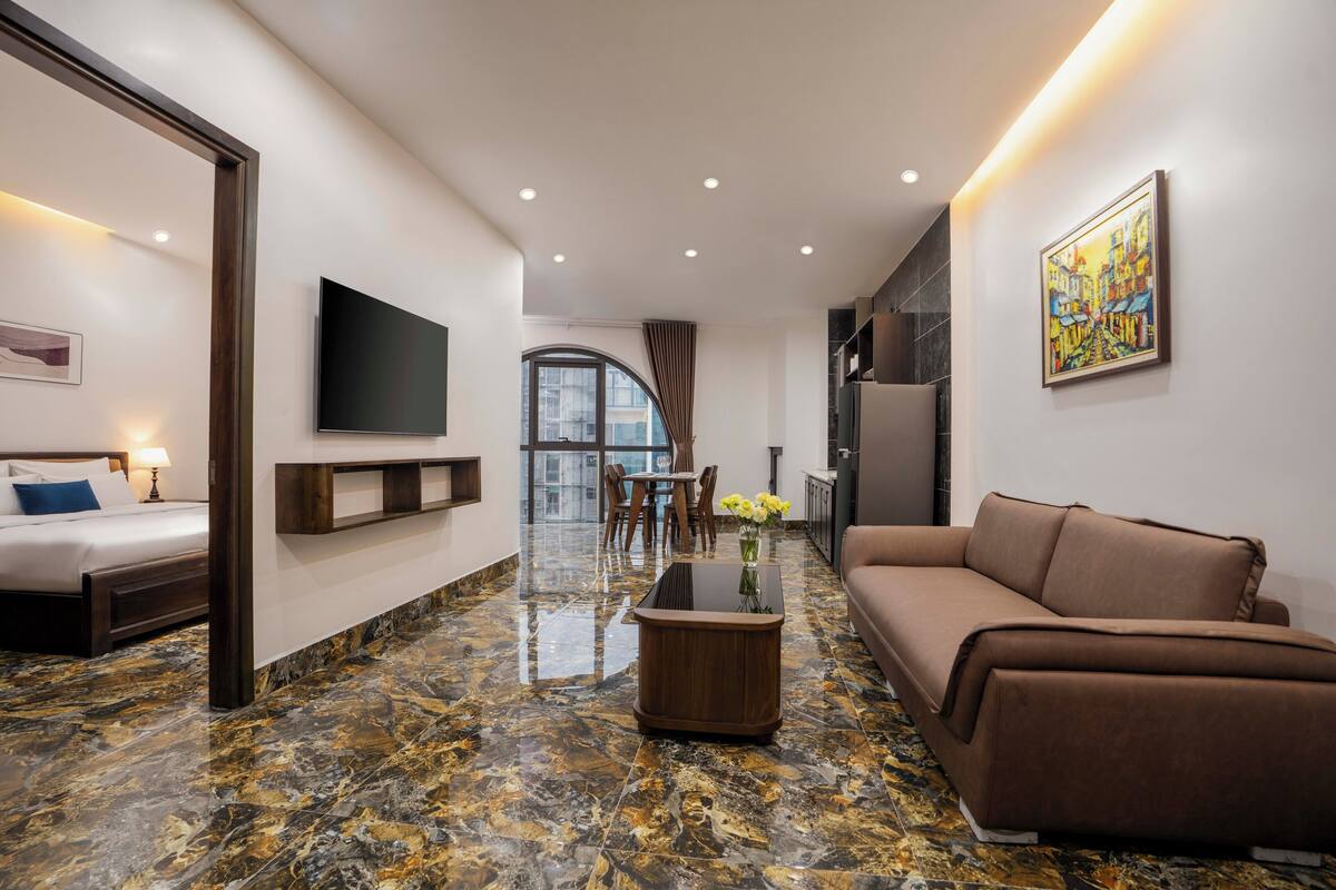 A modern hotel room with a bed, a sofa, a coffee table, and a TV.