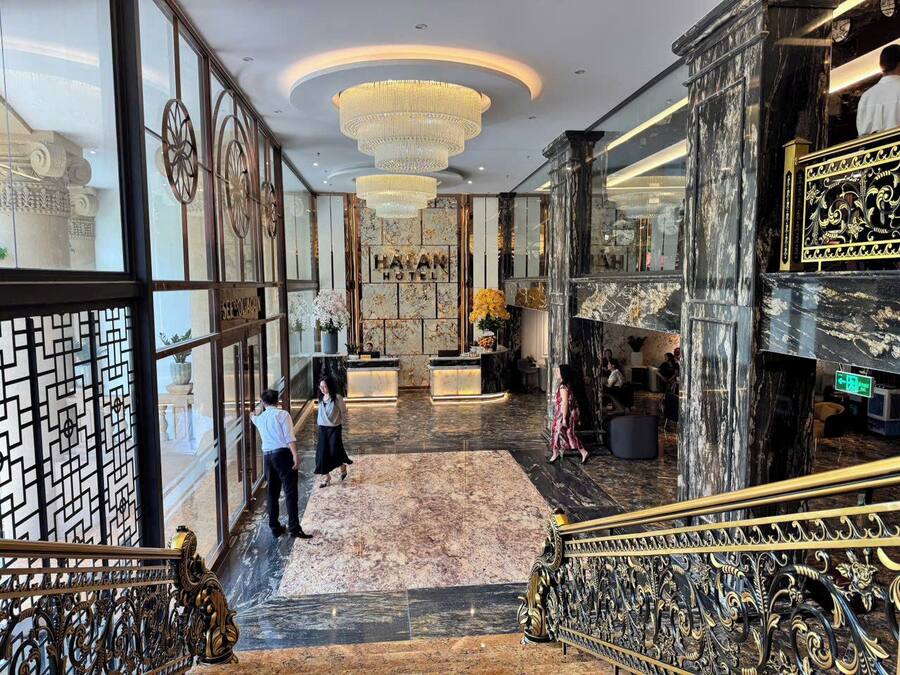Un amplio vestíbulo con suelo de mármol, una recepción y una escalera con barandales decorados.
