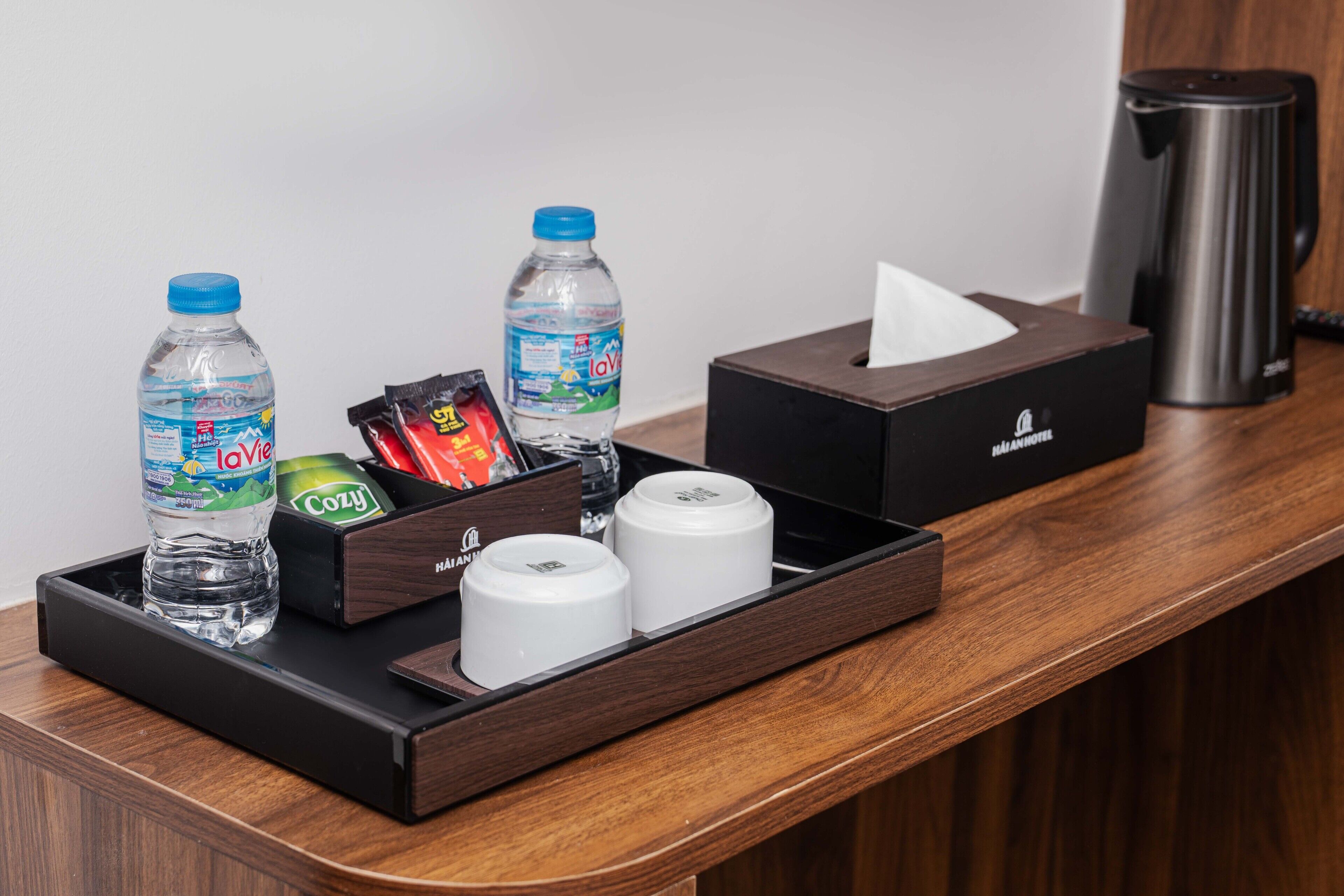 A hotel room's reception area with a tray containing two bottles of water, a box of tissues, a box of snacks, and a coffee maker.