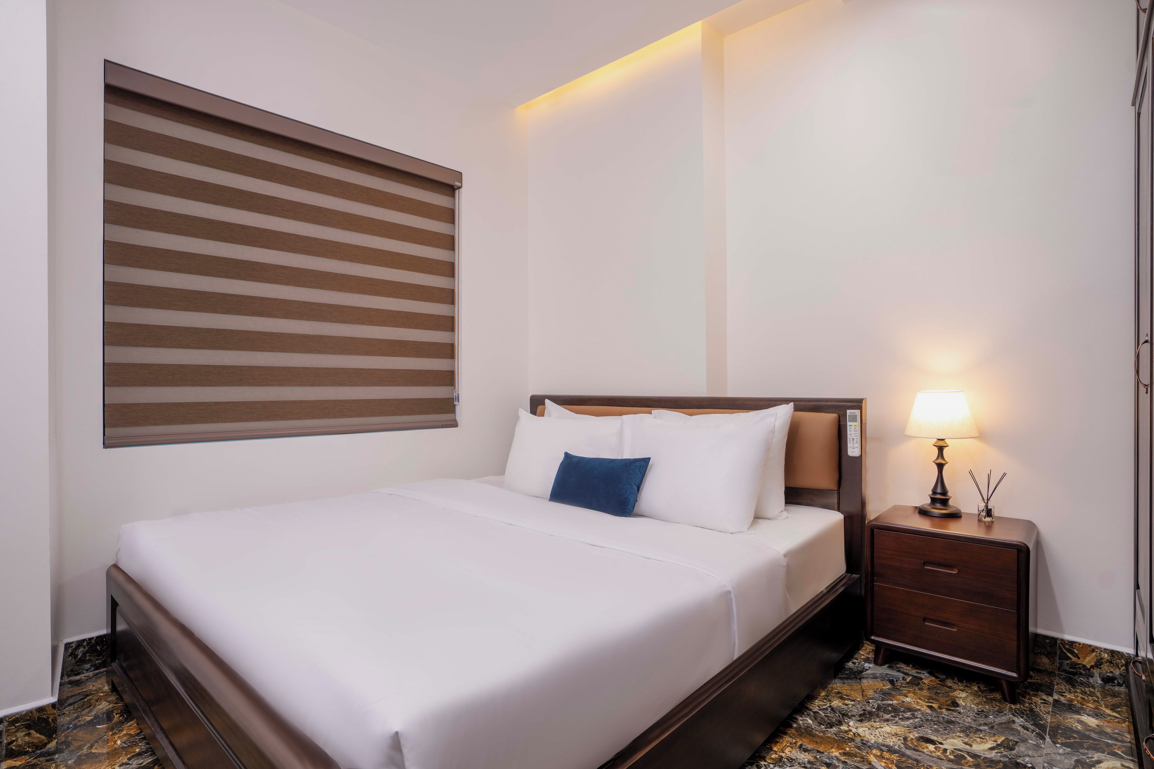 Una habitación de hotel con una cama, una mesita de noche con lámpara y una ventana con persianas.