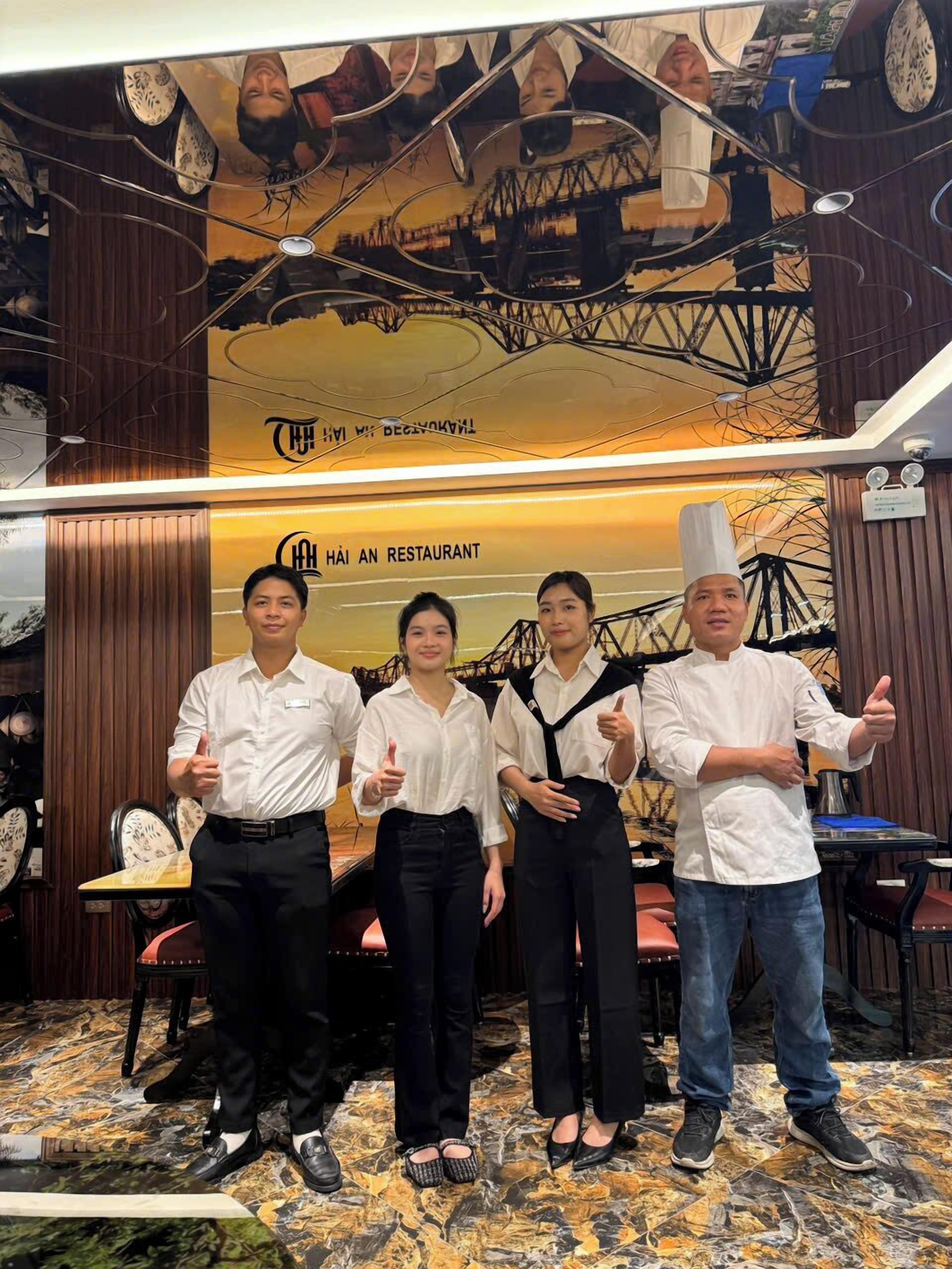A group of four people in a restaurant with a sign reading 'HÀI AN RESTAURANT' and a decorative ceiling.