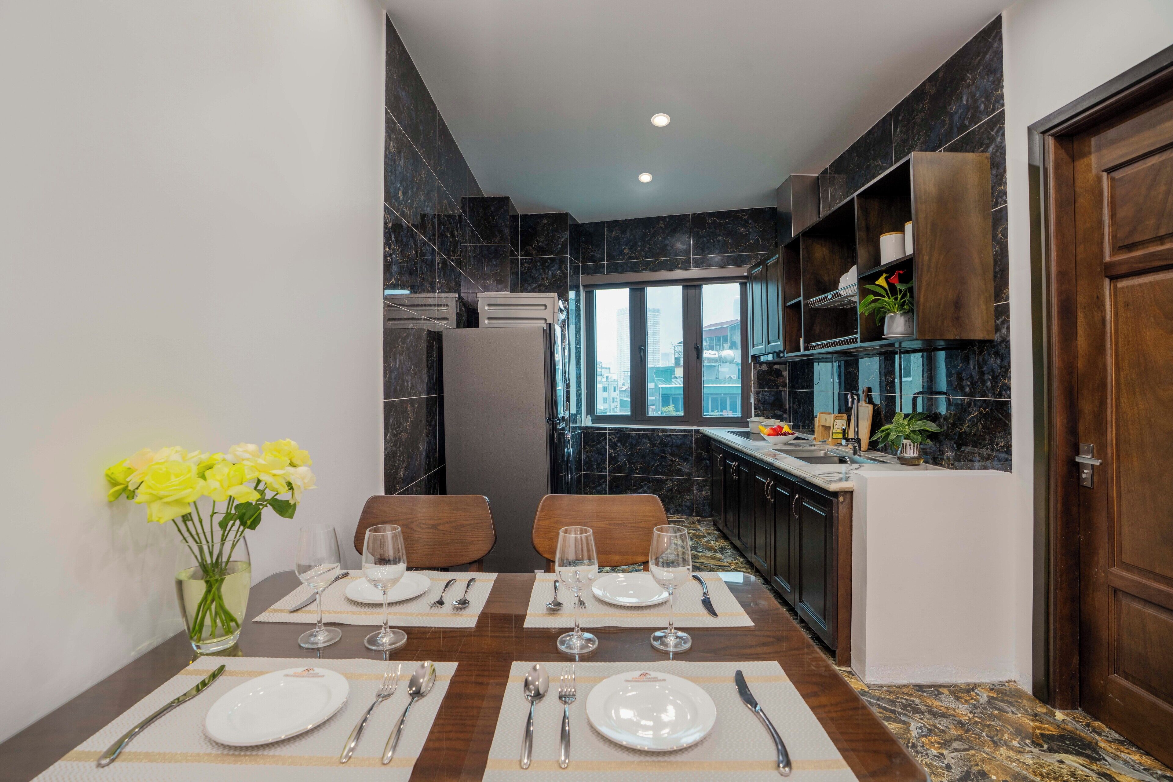 Una cucina moderna con piastrelle in marmo scuro, un'area pranzo con tavolo imbandito per quattro persone e vista sulla città dalla finestra.