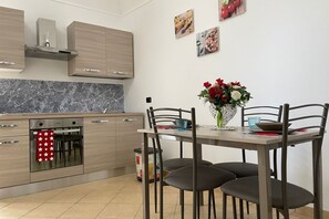 A modern kitchen with wooden cabinets, a built-in oven, and a dining table with chairs. - Sweet Sun Studio Apartment – Cozy Comfort Just Minutes from Sorrento ☀️🏡 (Meta)