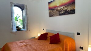 A bedroom with a bed, pillows, a nightstand, a lamp, a window with curtains, and a wall-mounted picture. - Sweet Sun Studio Apartment – Cozy Comfort Just Minutes from Sorrento ☀️🏡 (Meta)