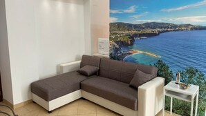 A room with a large window, a white sofa, a small table with a bowl, and a wall-mounted device. - Sweet Sun Studio Apartment – Cozy Comfort Just Minutes from Sorrento ☀️🏡 (Meta)
