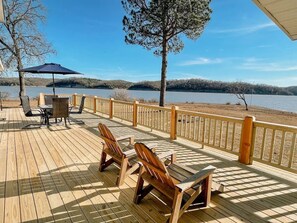 A wooden deck with chairs and a table, overlooking a lake. - The Lakehouse at Hidden Cove (Fairland)