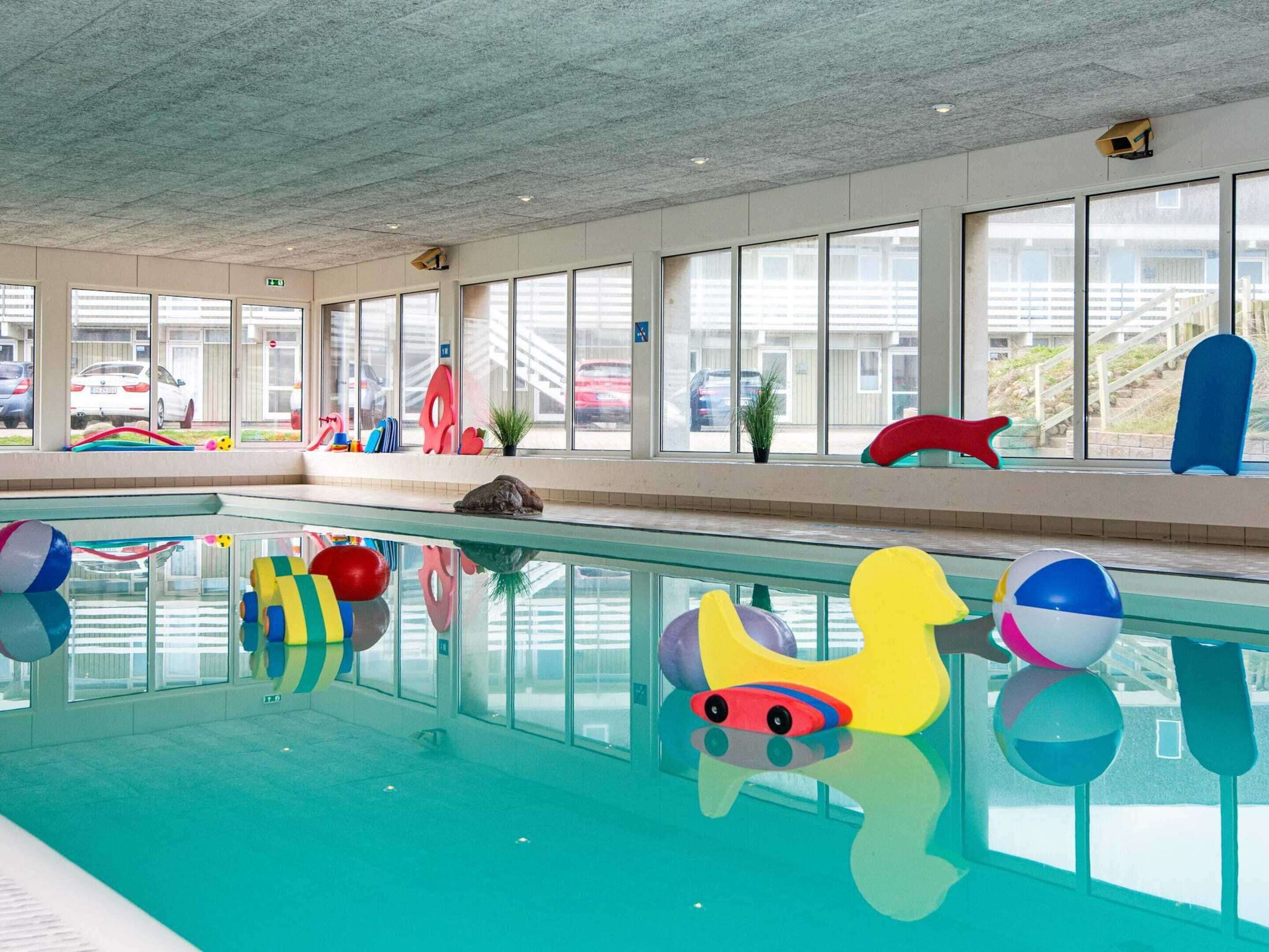 An indoor swimming pool with colorful play equipment and large windows.