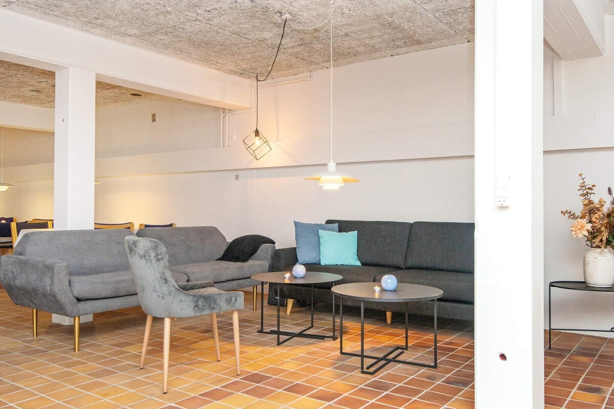 Ein modernes Wohnzimmer mit einem grauen Sofa, einem passenden Sessel, zwei kleinen runden Tischen und einer hängenden Leuchte.