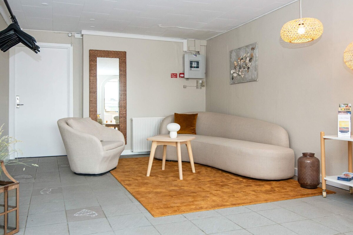 A modern living room with a beige sofa, a round wooden side table, and a brown rug.