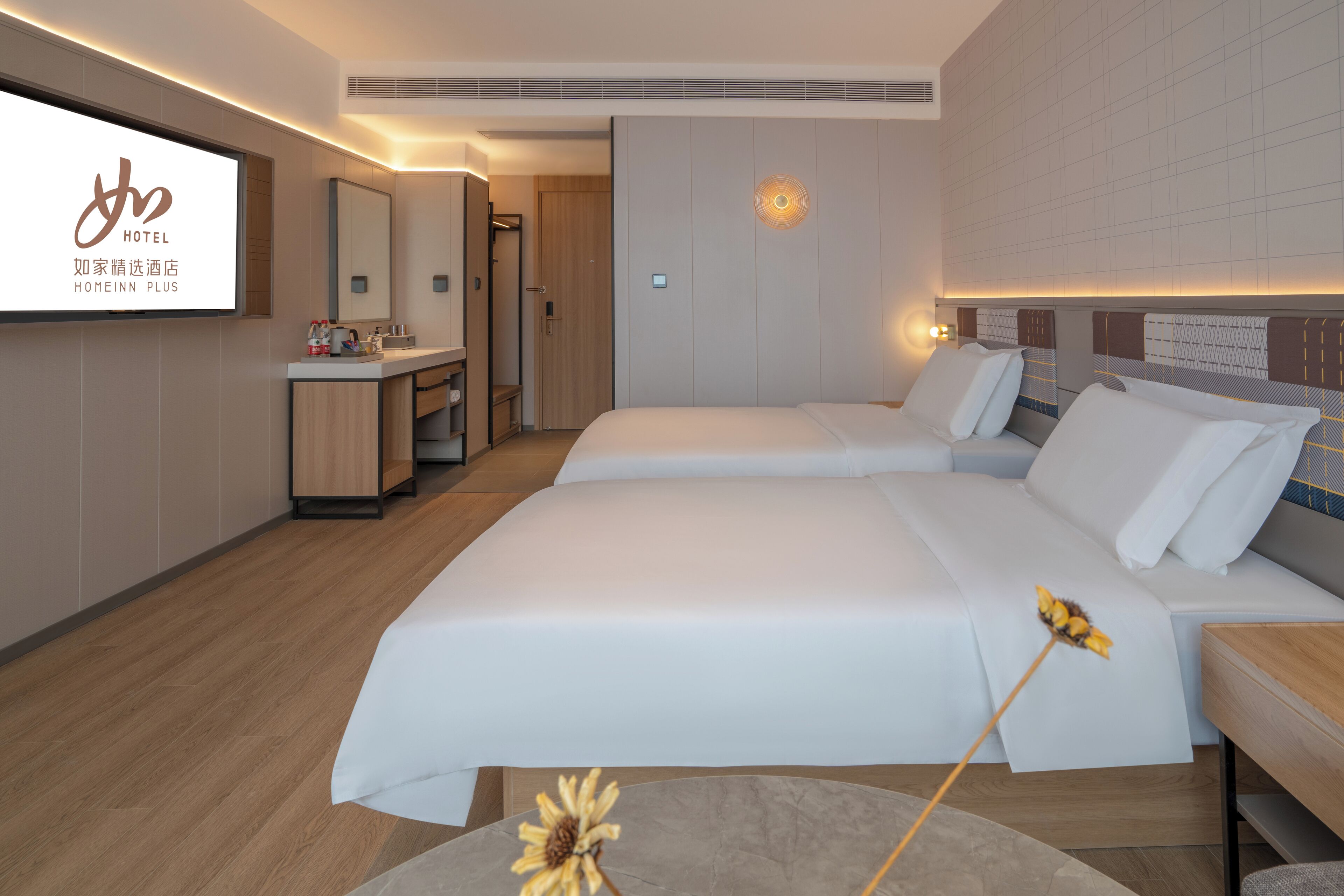 Habitación de hotel con dos camas, baño y un televisor que muestra el logotipo del hotel.