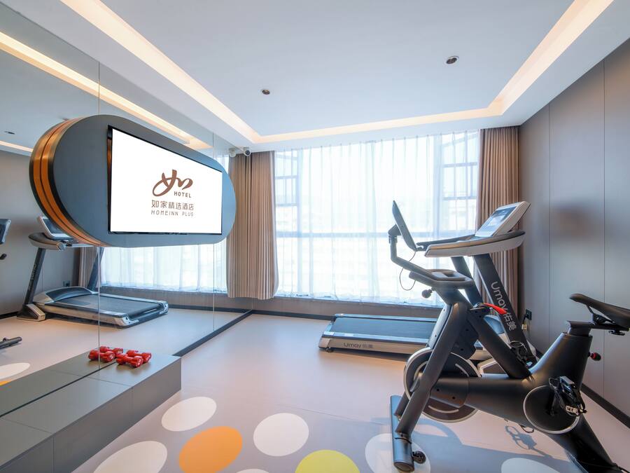 Una habitación de hotel moderna con un televisor grande, equipo de ejercicio y vistas a la ciudad.