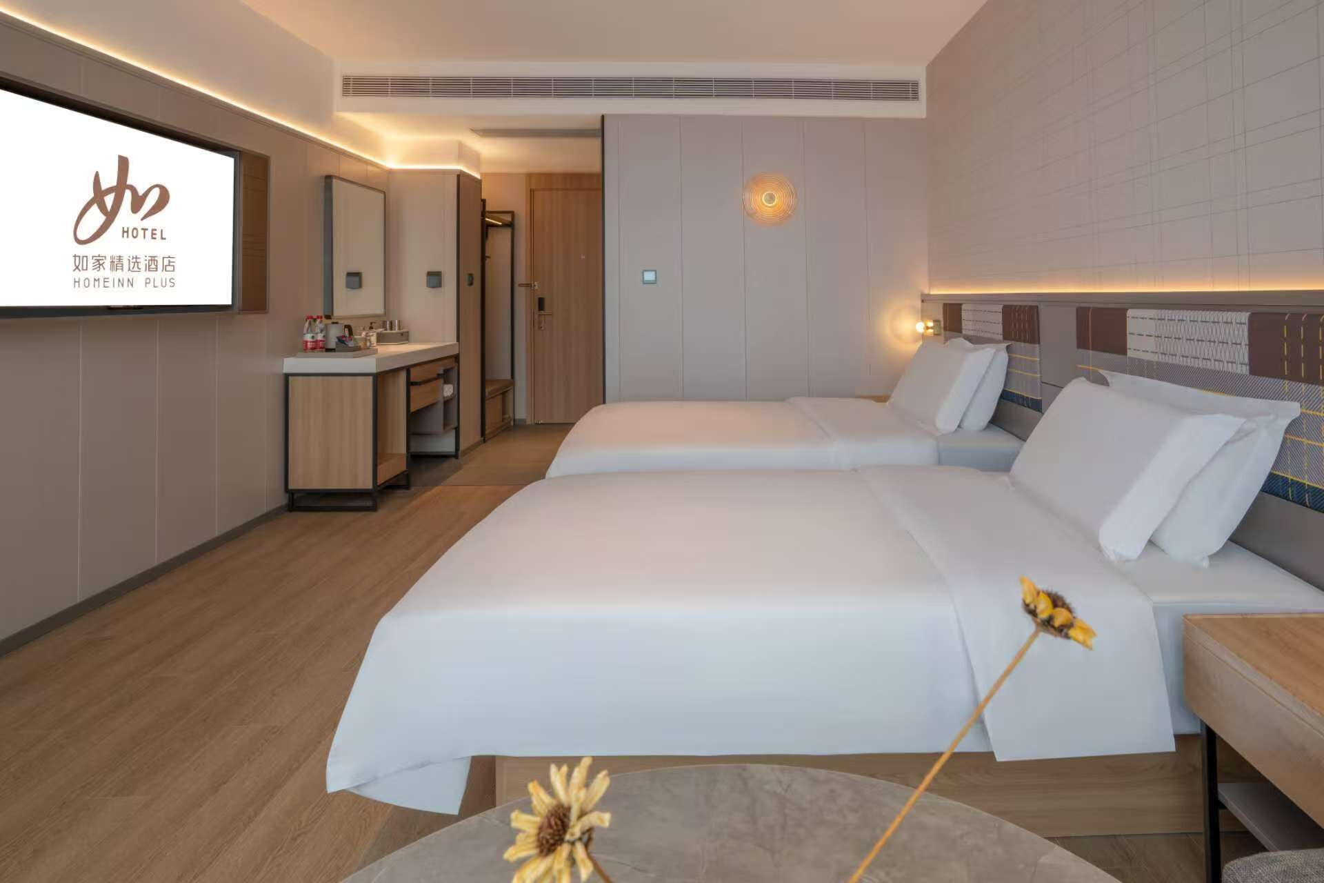 A hotel room with two beds, a desk, a mirror, and a TV screen displaying the hotel name.